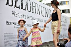 Frau mit Kindern vor Plakatwand: »Belohnung…«.